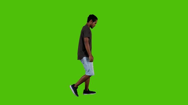 Upset young man walking annoyed and angry, a full side shot over a green background.