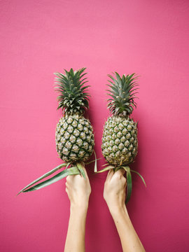 Crop woman showing pineapples on pink