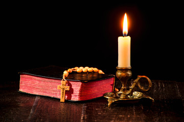 A rosary on the book, and a lit candle in a candlestick