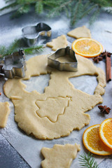 Preparation of Christmas cookies in the form of Christmas trees, fresh dough, spices scattered on the table, cinnamon, orange slices, nuts. Diet. Close-up background.