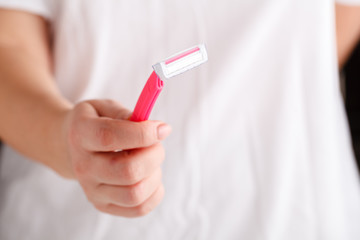 Disposable shaver in female hand on abstract blurred white background. Epilation, razor hair removal and skin care concept