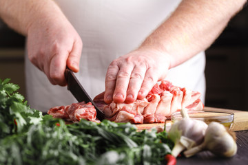 Man cutting rack of lamb on wooden board at restaurant kitchen. Chef preparing fresh meat for...