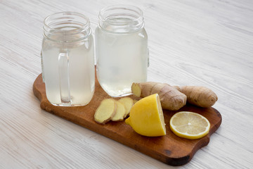 Glass jars of ginger tea with ingredients on wooden board over white wooden background, side view. Closeup.