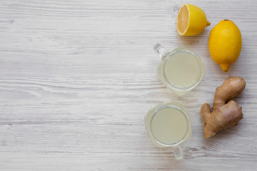 Glass jars of homemade ginger tea with lemon over white wooden background, overhead view. Flat lay, from above, top view. Copy space.