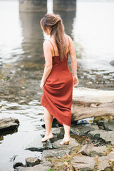 A young girl in a light dress walks on the stones to the water