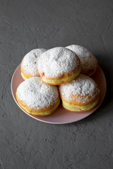 Homemade sweet donuts with powdered sugar on pink plate over concrete background, side view. Closeup.