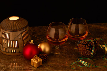 pair of glasses of liquor on decorated Christmas table with candle lamp and black background