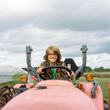Boy in plaid flannel shirt sits on a tractor, pretending to drive