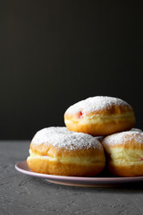 Homemade donuts with powdered sugar on pink plate, side view. Close-up.