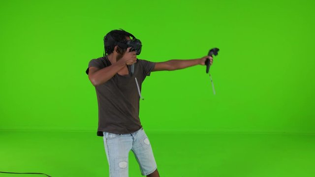 Shooting arrows happily using a longbow in a VR video game by a young man over a green screen, casual look, medium shot.