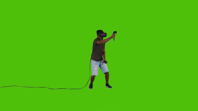 First person shooting with guns in a VR video game by a young man over a green screen, casual look, long shot.