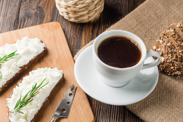 Breakfast with homemade sandwiches with cream-cheese and coffee on a wooden table.