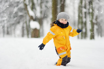 Fototapeta na wymiar Cute little boy in yellow winter clothes walks during a snowfall