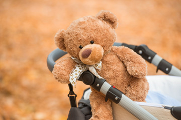 Soft toy bear in a baby carriage in the fall. Landscape in warm colors