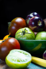 Multicolored assortment of French fresh ripe tomatoes in green bowl on blue wooden table, dark key