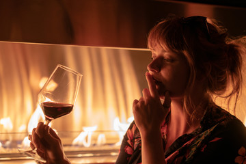 Beautiful ginger girl drinking a glass of red wine near a fire pit