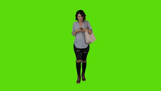 using an app happily while walking by a young woman over a green screen. casual look long frontal shot.