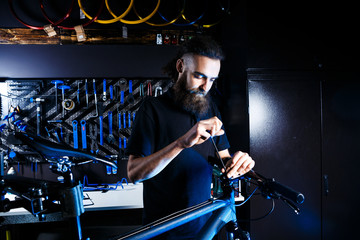 Obraz na płótnie Canvas Theme sale and repair of bicycles. Young and stylish with a beard and long hair, a Caucasian man uses a tool to set up and repair a bike in a store. Business owner at work