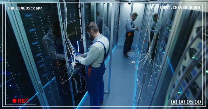 Wide shot from surveillance cctv camera of people working in a data center server room with rows of server racks checking the equipment and discussing their work.