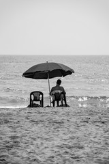 Alone man stting on the beach under umbrella, sea background.