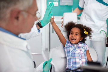 Cheerful young girl in dental chair making joke with male dentist