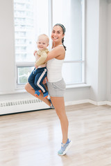 Fototapeta na wymiar Young woman with child doing workout in gym class to loose baby weight. Child-friendly fitness for mothers with kids toddlers. Lifestyle concept of parent activity.