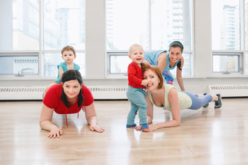 Group of three young women with children doing workout in gym class with instructor to loose baby weight. Child-friendly fitness for mothers with kids toddlers. Lifestyle concept of parent activity