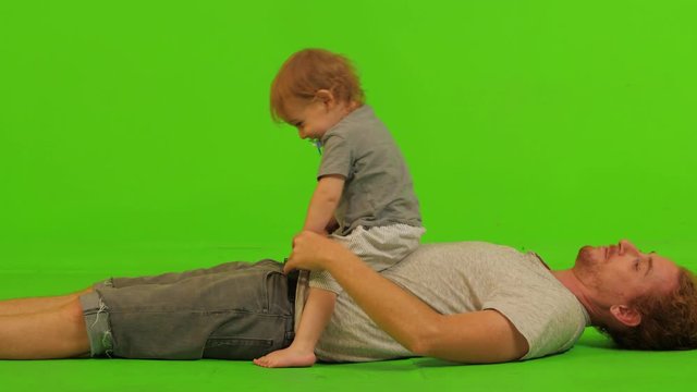 A dad plays with his cute toddler son over a green screen, clapping hands in a medium long shot.