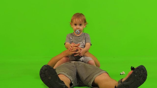 A dad plays with his cute toddler son over a green screen, frontal medium long shot.