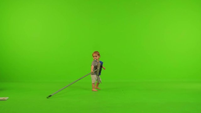 A toddler plays and spins a broom happily over a green screen.