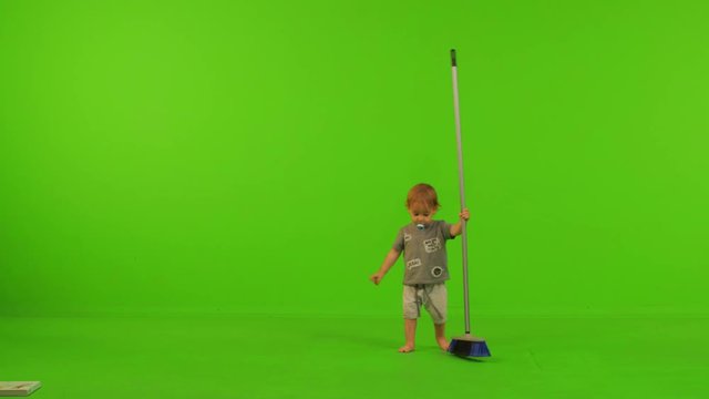 A toddler plays and spins a broom happily over a green screen.