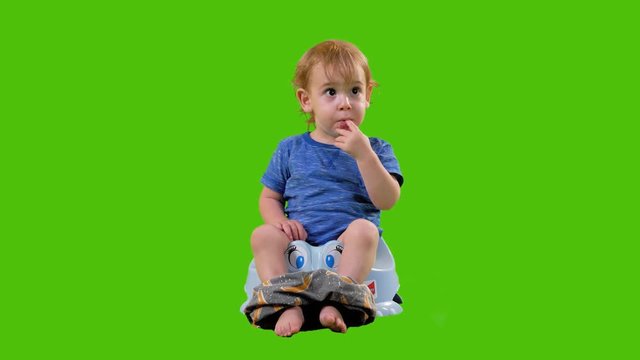 Cute little toddler sits on a potty, eats and laughs in a full shot over a green screen.