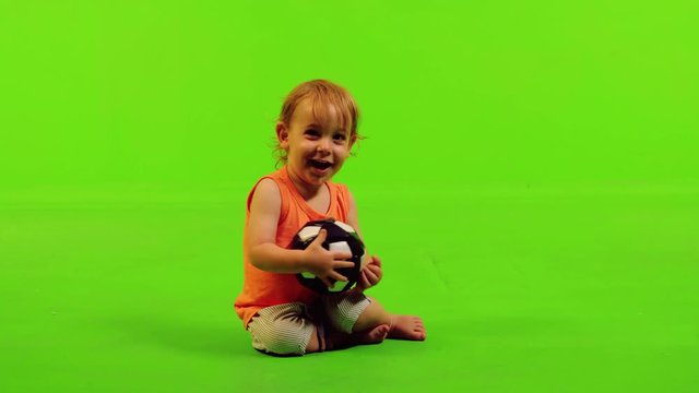 Cute little toddler sits and play with a ball in a full shot over a green screen.