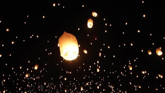 A person grabbing and letting go of a lantern sending it off into the night sky. A lantern lit by fire flys slowly off into the air. Close up up a persons hands holding a lantern.
