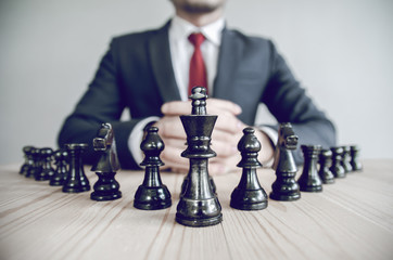 Retro style image of a businessman with clasped hands planning strategy with chess figures on an...