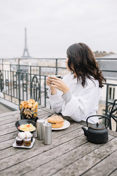 Young woman having breakfast on terrace with the Eiffel Tower view