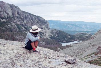 Young woman wearing hat sitting on mountain ledge overlooking Rocky Mountain National Park