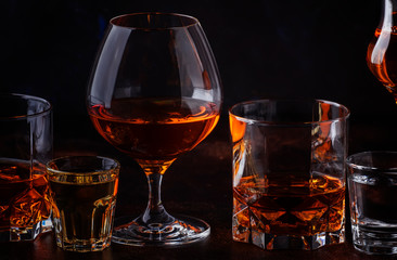 Set of strong alcoholic drinks in glasses and shot glass in assortent: vodka, rum, cognac, tequila, brandy and whiskey. Dark vintage background, selective focus