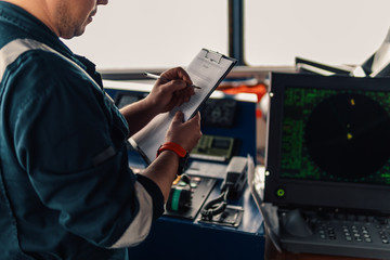 Marine navigational officer or chief mate on navigation watch on ship or vessel. He fills up checklist. Ship routine paperwork