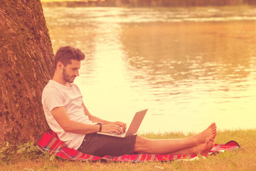 man using a laptop computer on the bank of the river