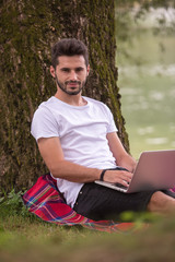 Obraz premium man using a laptop computer on the bank of the river