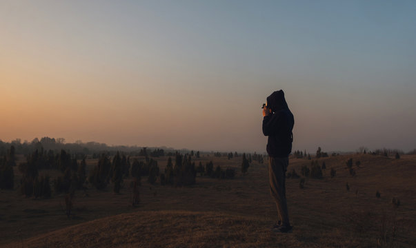 Fototapeta Look from behind on man  standing in front of wasteland with camera