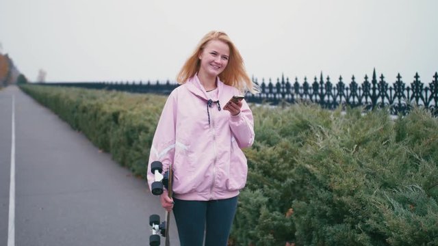 Pretty beautiful blond hipster woman with skateboard longboard using her smartphone cell phone for browsing, sms or chatting