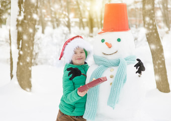 portrait of smiling boy in red christmas hat holds gift box and hugs snowman