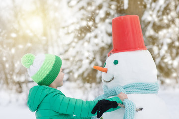 boy knots a scarf on a snowman