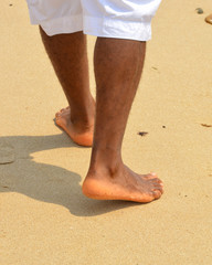 African american man walks on a sand beach. Close up of male feet and golden sand. Beach walk. Summer activity. Beautiful holiday background