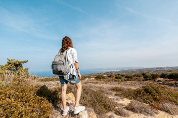 Happy young woman traveler stands on a hill overlooking the sea, traveling in Greece