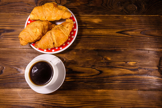 Cup of dark coffee and croissants on wooden table. Top view