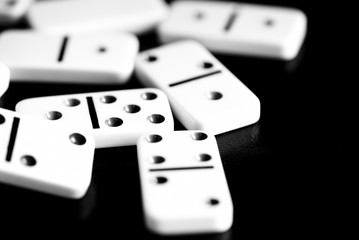 Dominoes are scattered on a dark surface close up. Black and white