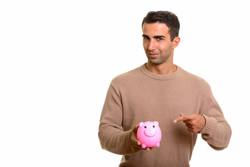 Portrait of young handsome Persian man with piggy bank